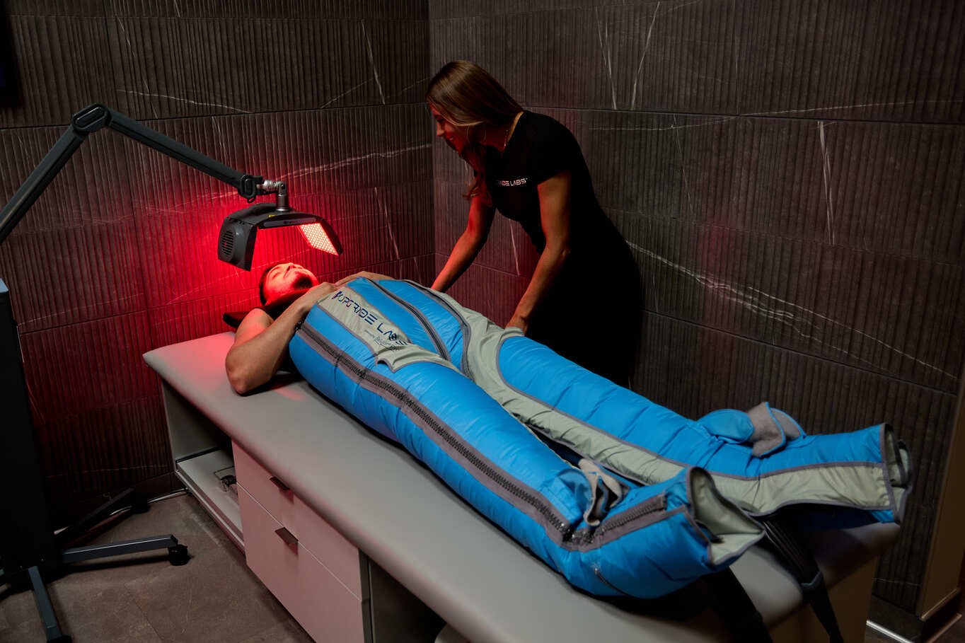 Man lying down in The Big Squeeze compression therapy system while a staff member assists him at Upgrade Labs.