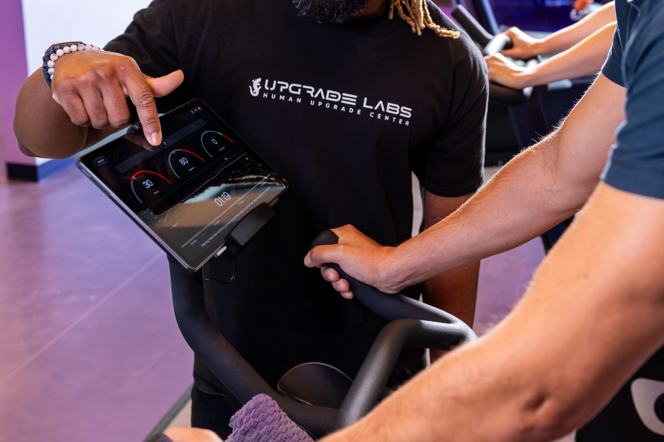Up close of the AI Adaptive Bike screen with a man riding and a staff member pointing at the display.