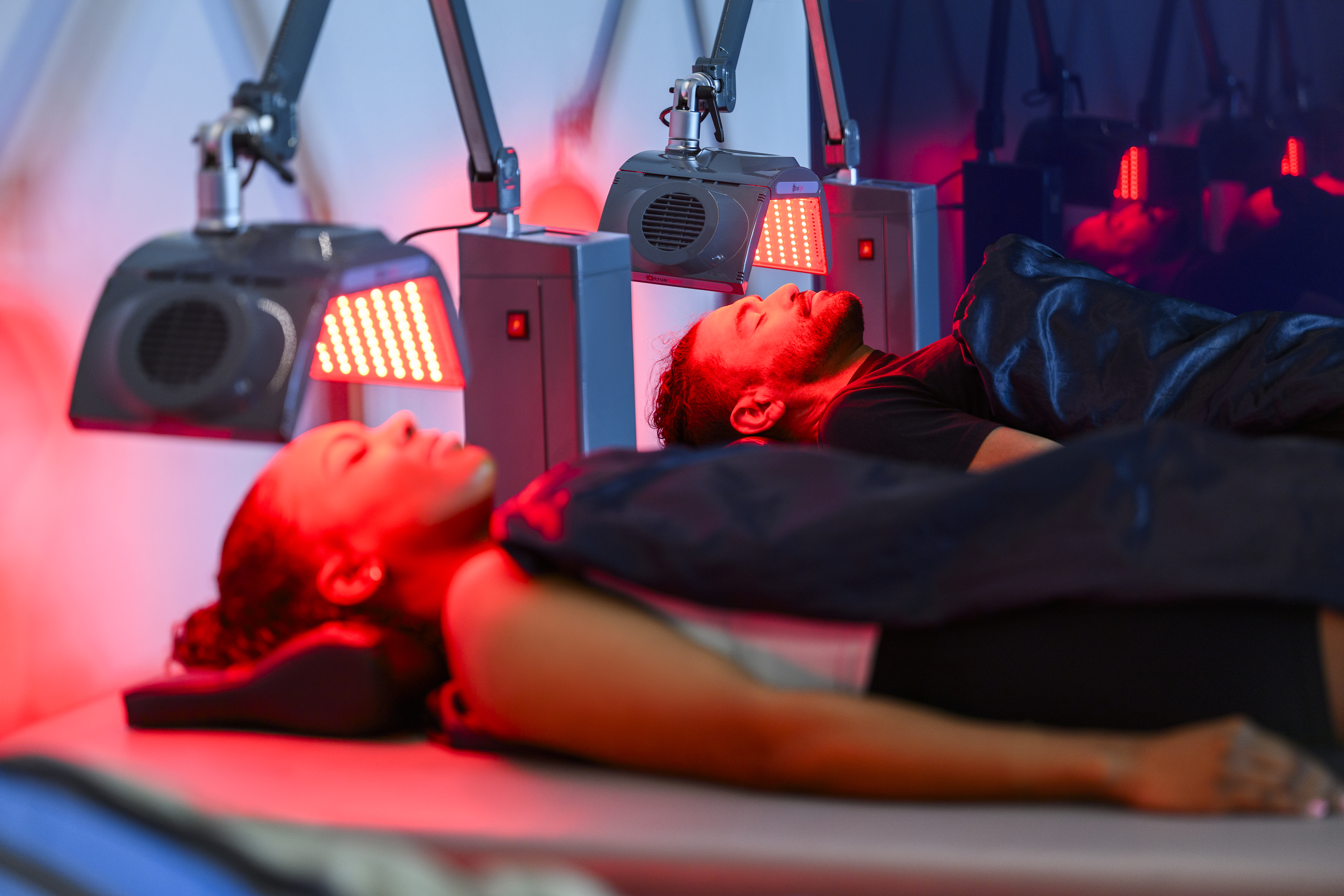 Woman lying under a PEMF blanket with a man resting farther away under another PEMF blanket.