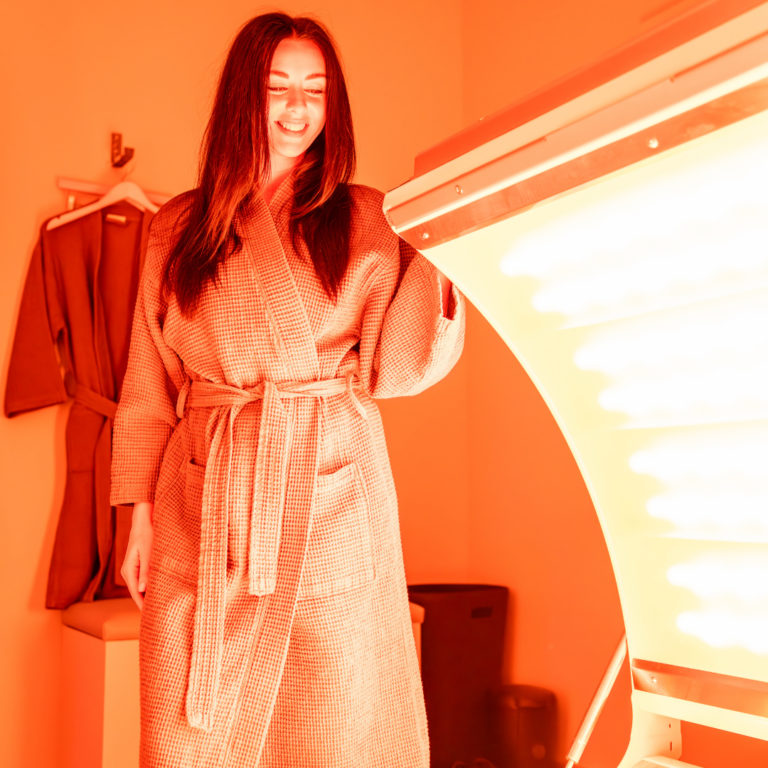 A woman in a robe is standing next to the REDcharger™ at Upgrade Labs, looking at the inside the machine and preparing to get in.