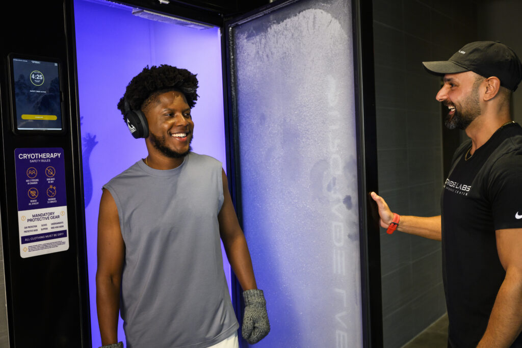 Man stepping out of a cryotherapy chamber smiling as a staff member opens the door.