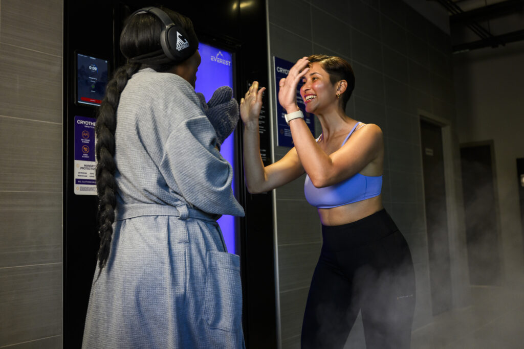 Two women high-fiving outside a cryotherapy chamber