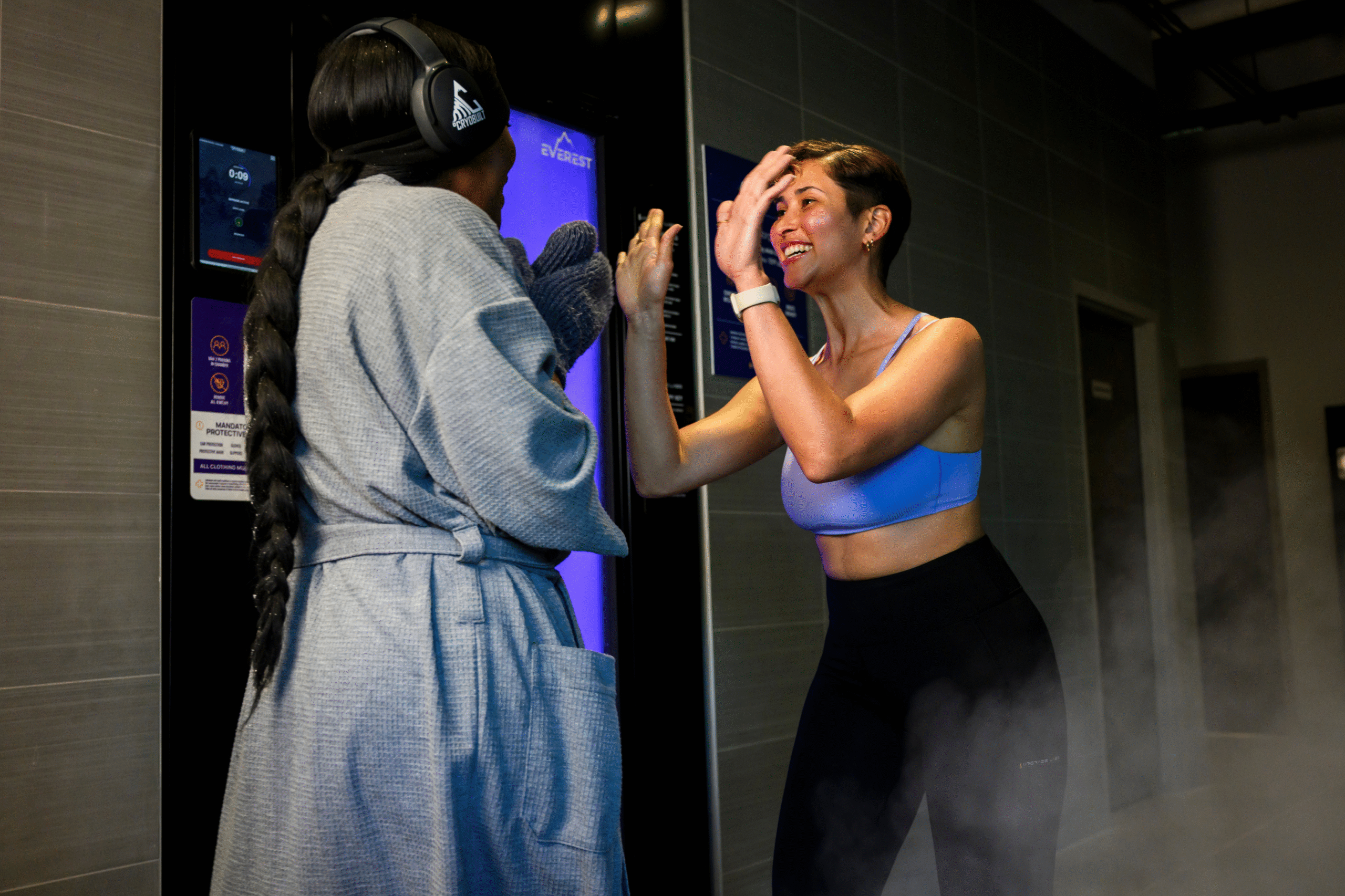 Two women high-fiving outside a cold therapy chamber