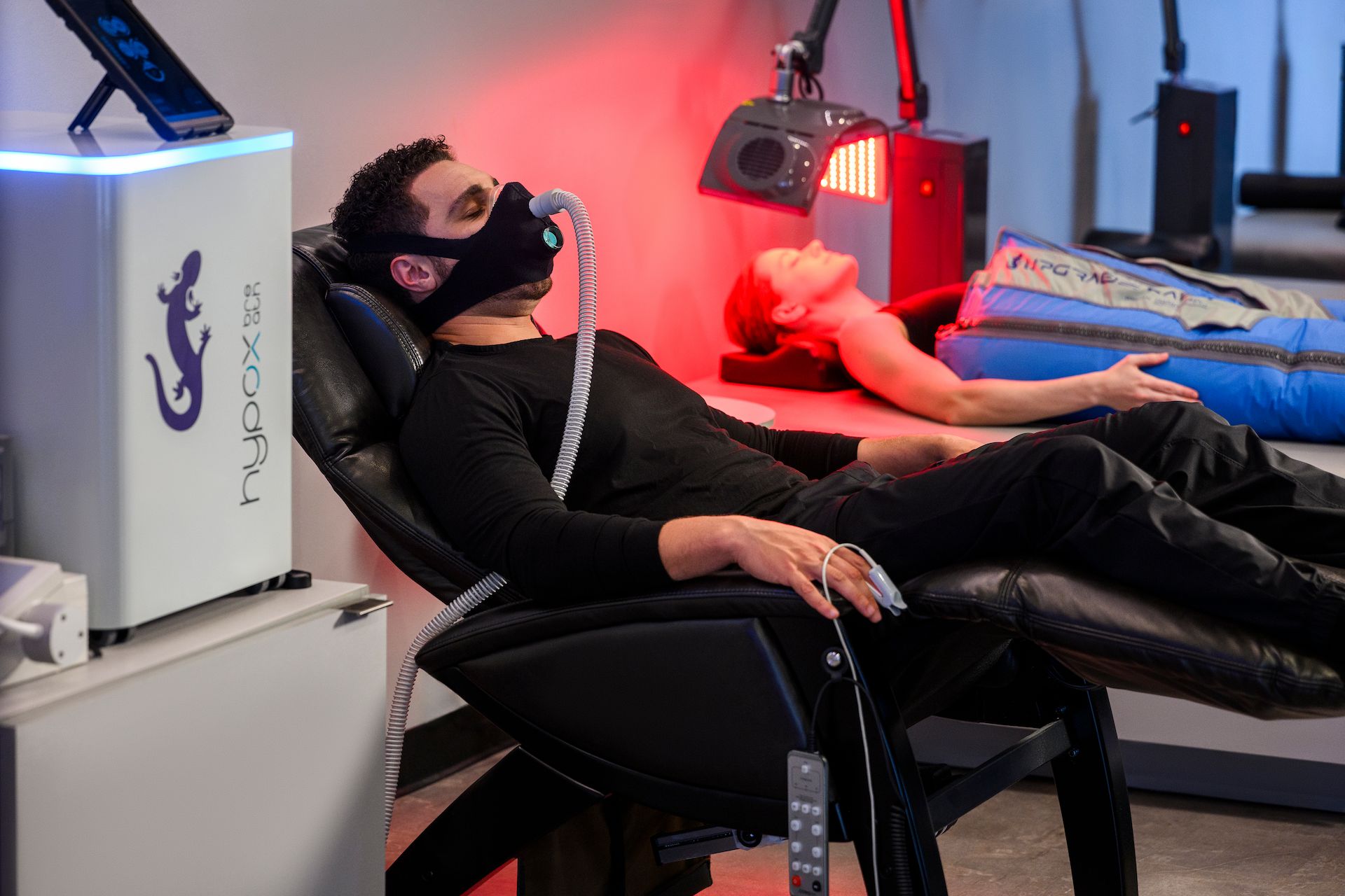 Man using the Metabolic Oxygen Trainer while a woman relaxes in the Big Squeeze
