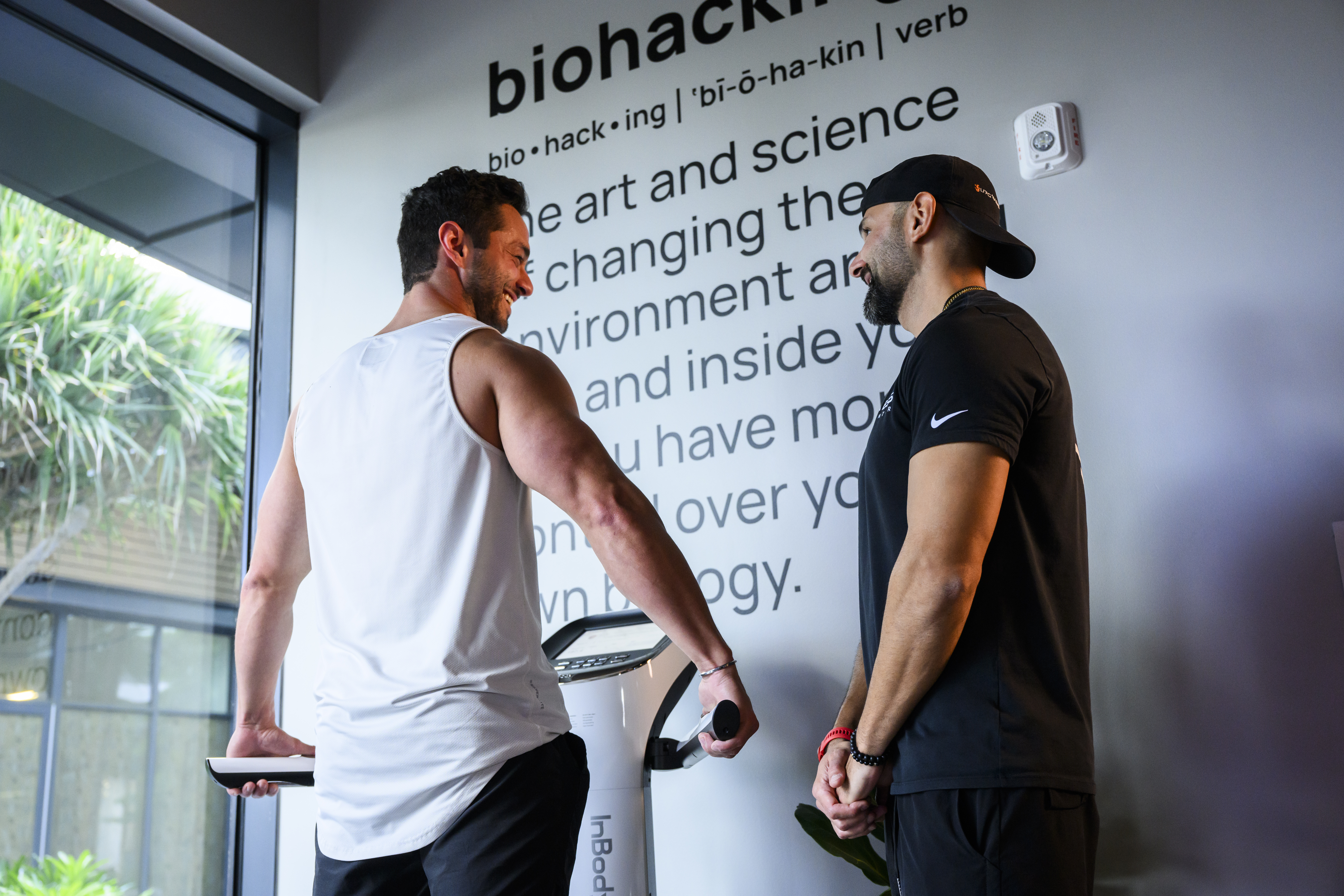 Man standing on the Cell Health Analysis platform while a staff member stands beside him, both smiling at each other as the staff member guides him through the process.