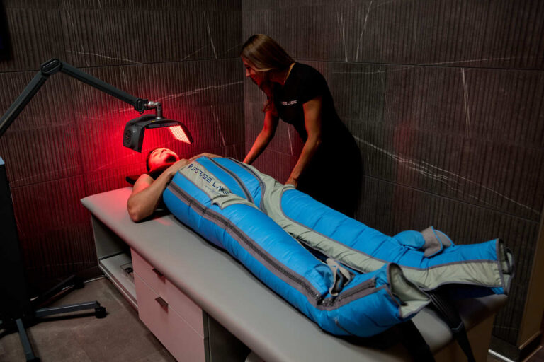 Man lying down in The Big Squeeze compression therapy system while a staff member assists him at Upgrade Labs.